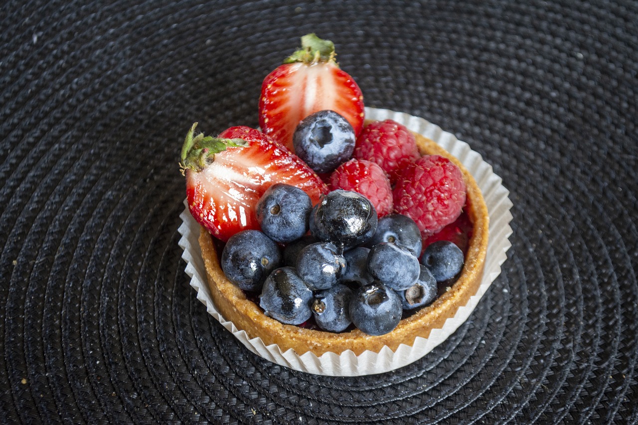 Crostata morbida alla frutta, decorata con fettine di frutta fresca e crema, su un tavolo di legno.
